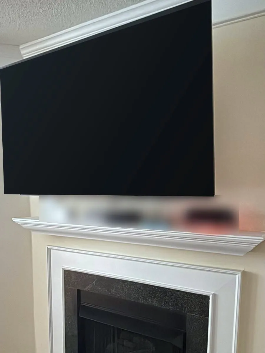 Large TV mounted above a white fireplace mantel with a dark stone surround