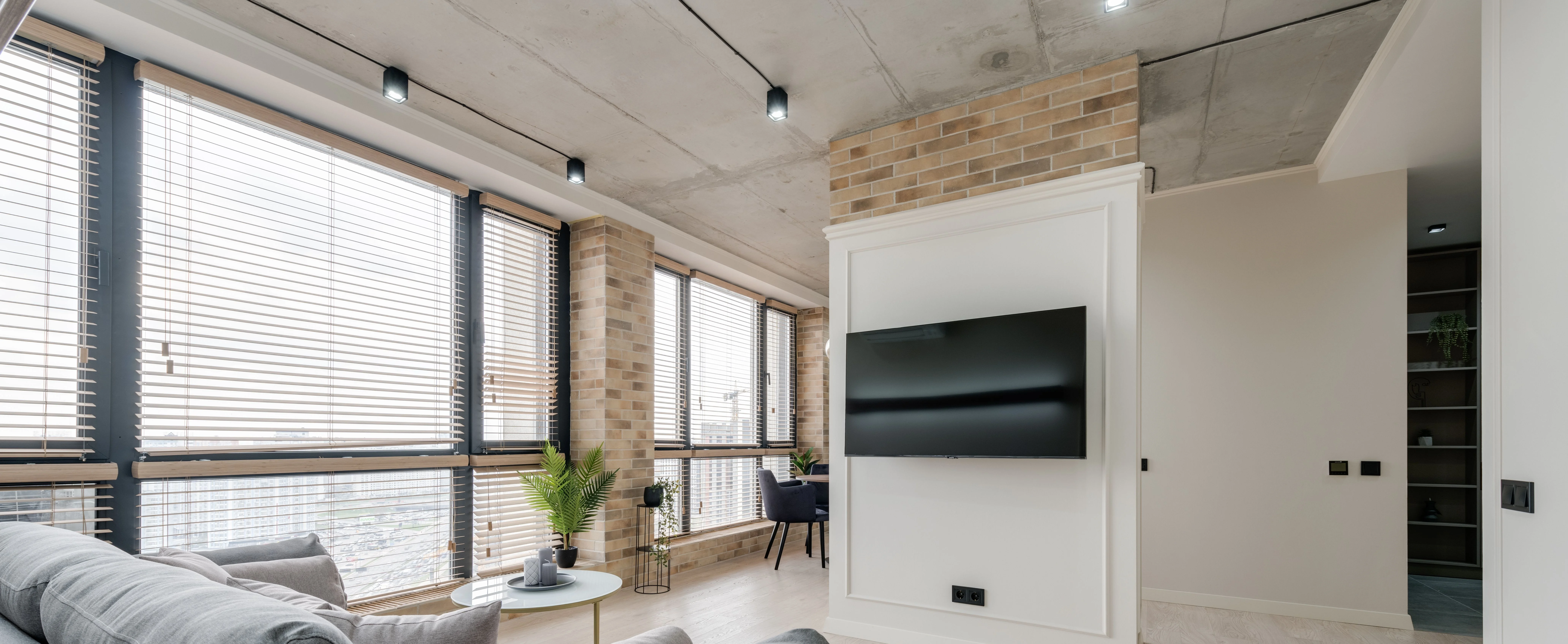 Bright living room with a wall-mounted television, warm oak console and a large window overlooking Los Angeles.