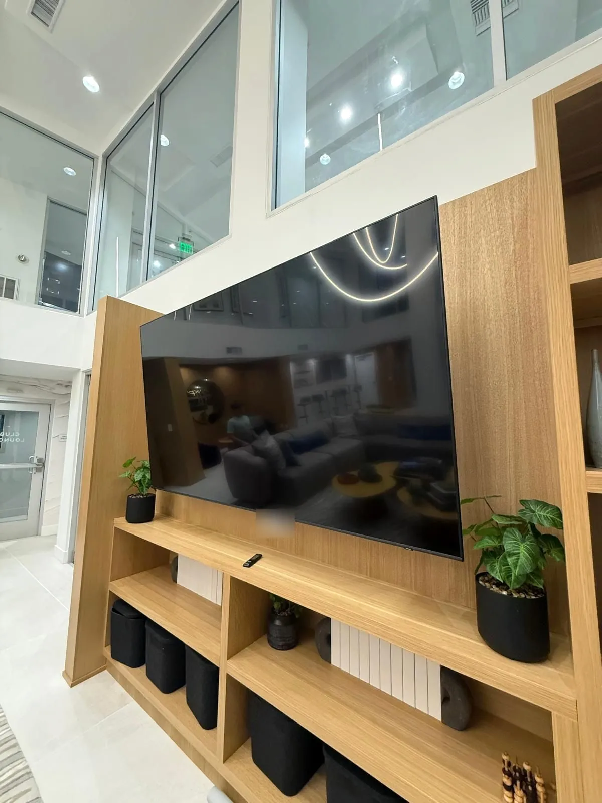 TV mounted on an oak media wall with open shelving below in a bright atrium