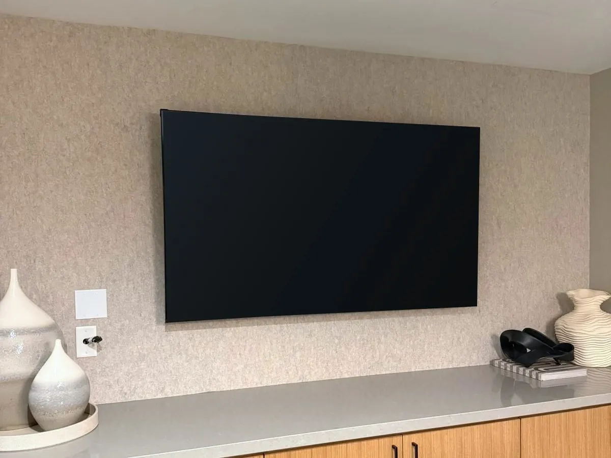 Large flat-screen TV mounted level on a textured wall above a stone-topped cabinet
