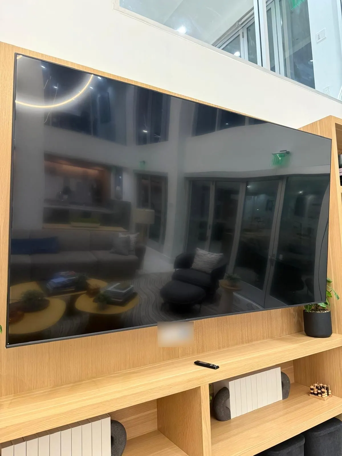 Extra-large TV mounted above built-in oak shelving in a double-height lobby